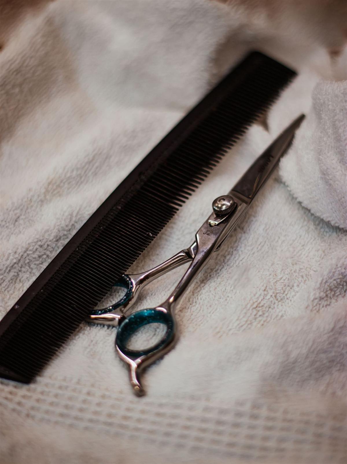Ciseaux de coiffeur à poignée turquoise et peigne noir posés sur une serviette