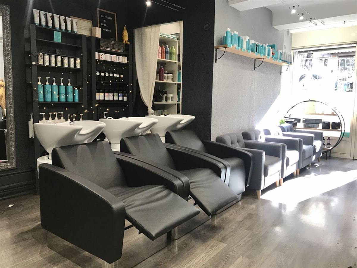 Trois postes de shampoing et fauteuils noirs, étagères de soins et fauteuils gris au salon